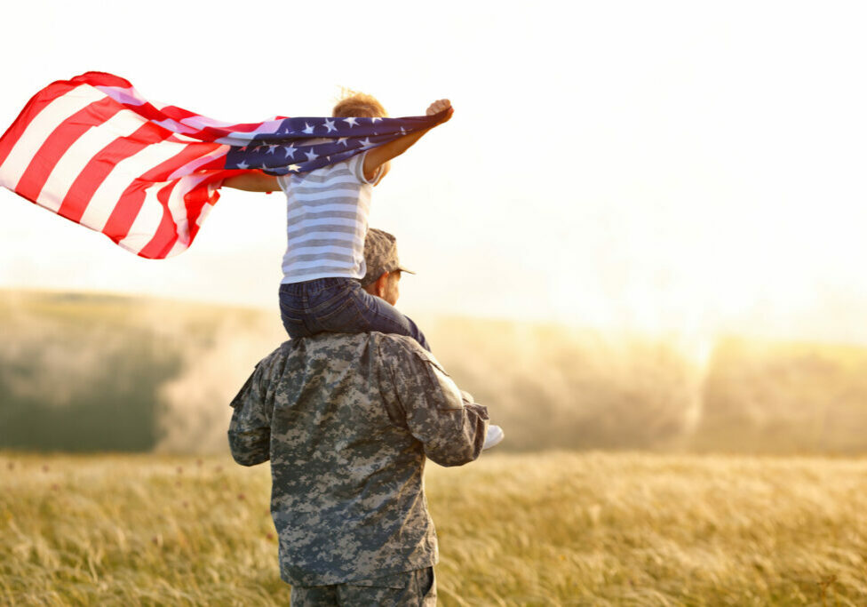 Excited child sitting with american flag on shoulders of father reunited with family